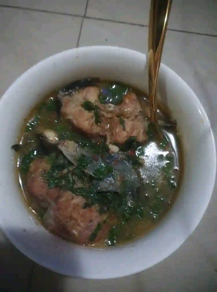 Bowl of Nigerian catfish pepper soup finished with green vegetables